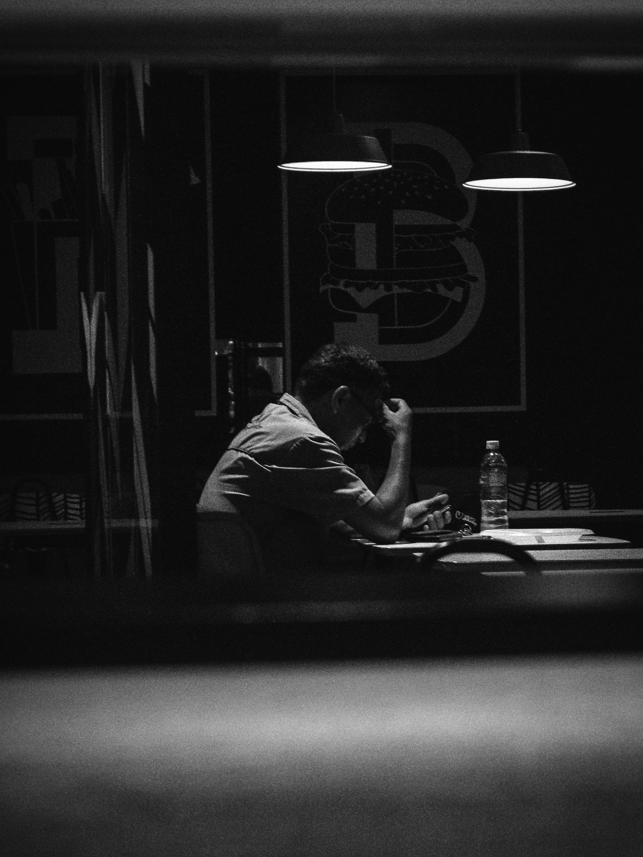 A man alone at his desk at night, head in his hand, the city lit up behind the curtains